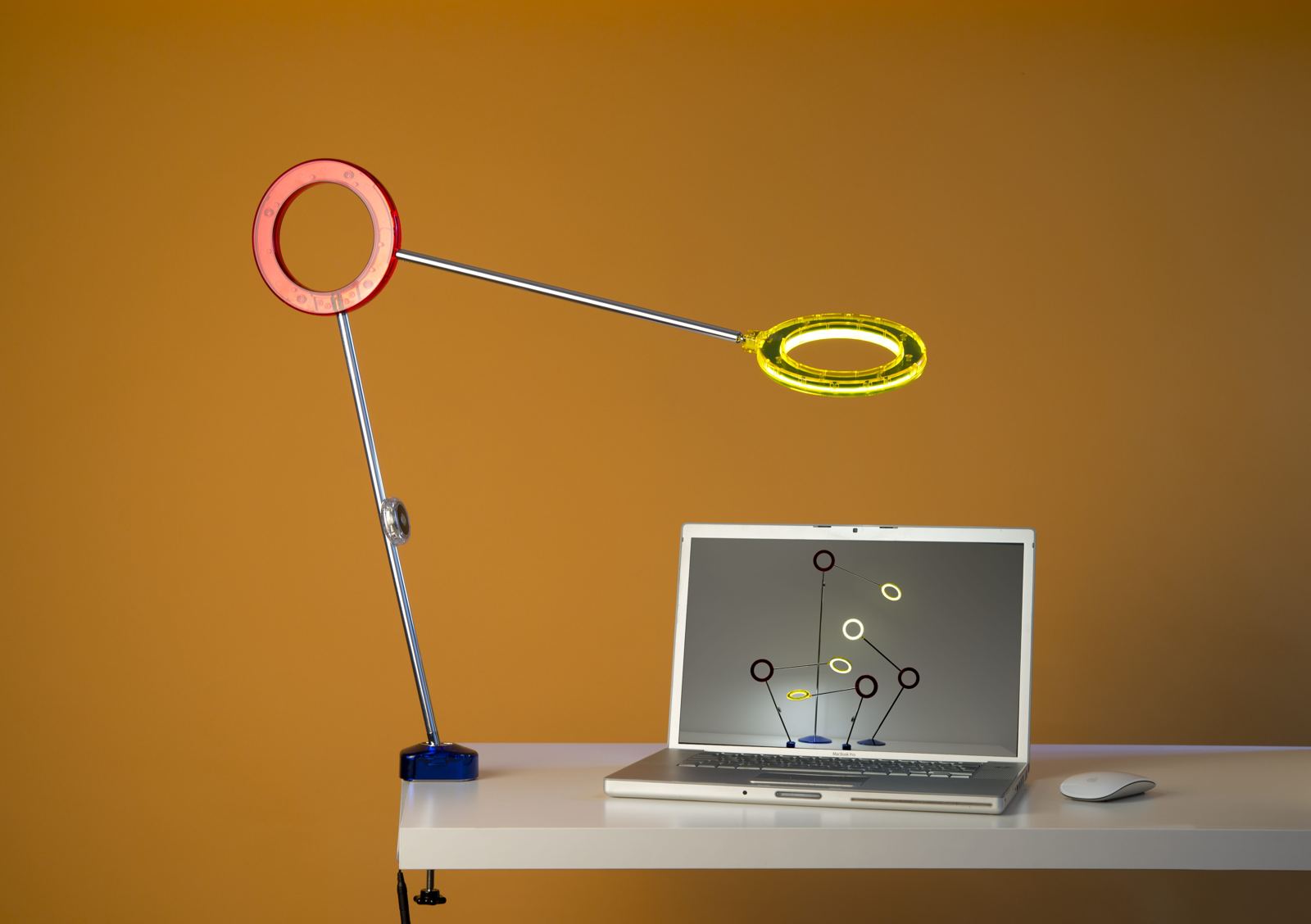 Amuleto desk lamp by RAMUN clamped to a desk edge beside a laptop, lighting the work area at close range